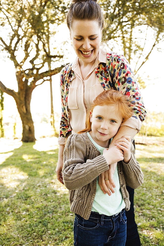 Portrait of mid adult mother with arm around daughter in park