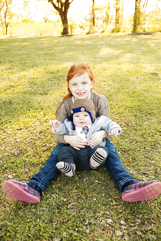 Portrait of girl and baby brother on grass in park