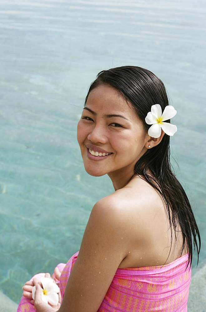 Portrait of smiling woman with frangipani flower in hair