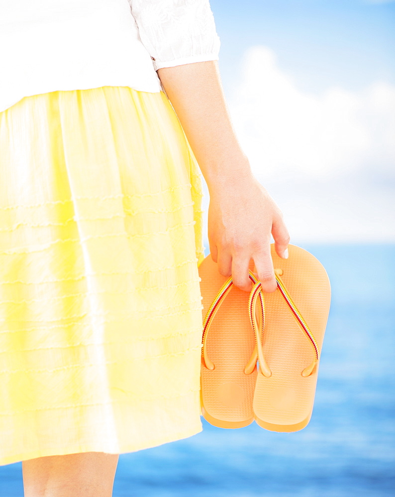 Studio Shot Mid section of woman holding flip-flops, rear view