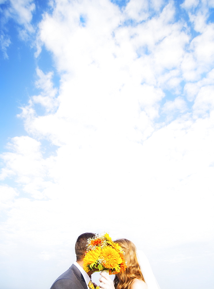 Portrait of married couple kissing behind bouquet