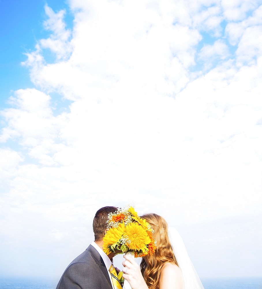 Portrait of married couple kissing behind bouquet