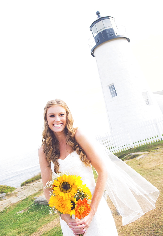 Portrait of smiling bride holding sunflower bouquet, lighthouse in background, USA, Maine, Bristol 