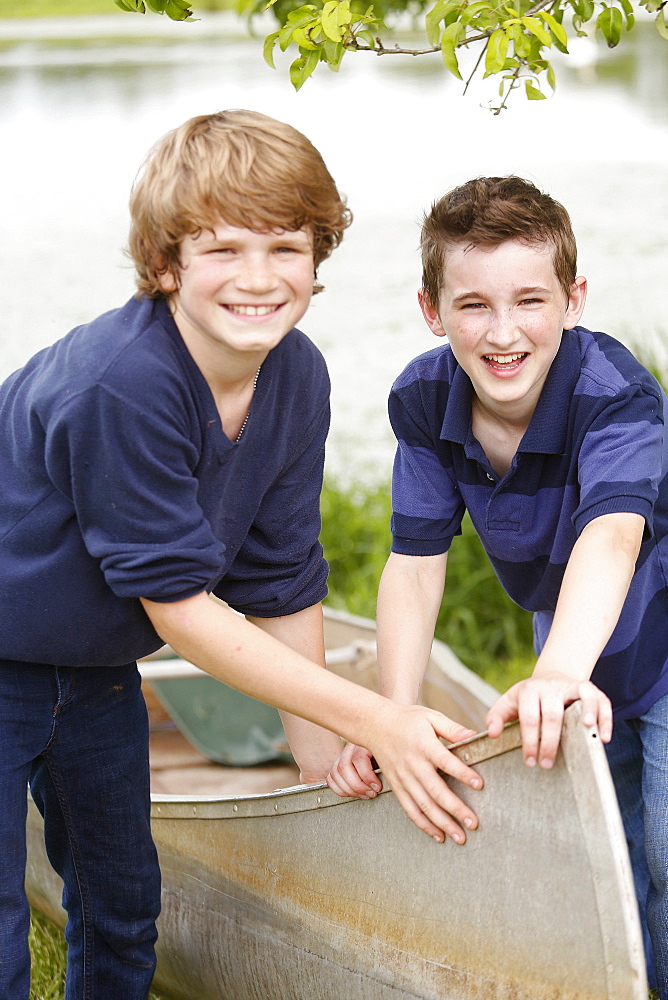 Two boys (12-13) posing with boat on grass near lake, USA, New Jersey, Old Wick 