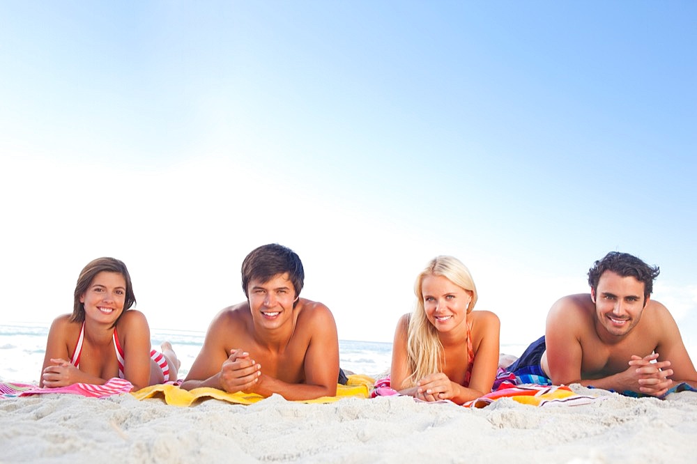 Two men and women lying on towels at the beach