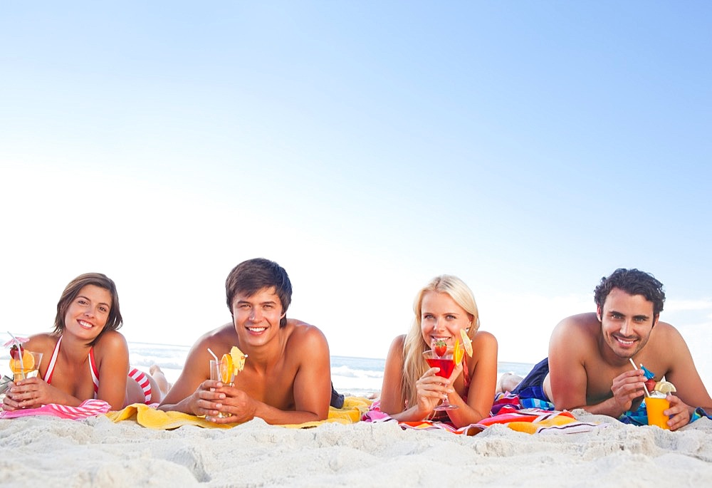 Four friends lying on towels while holding cocktails