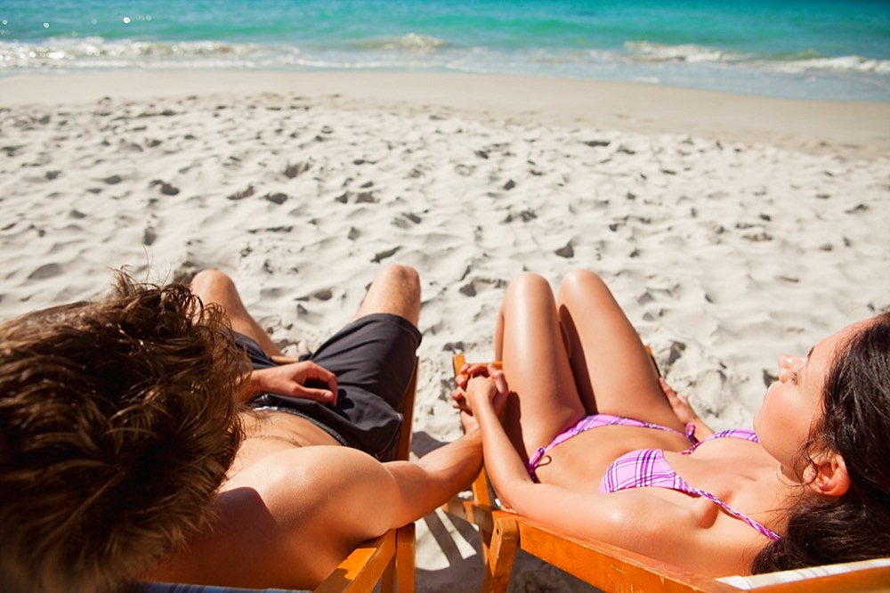 Rear view of a lovers in swimsuit taking a sunbath on deck chairs