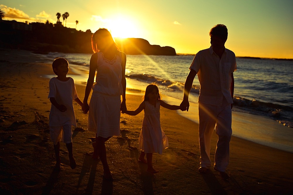 Family walking on the beach while the sun shines on their back