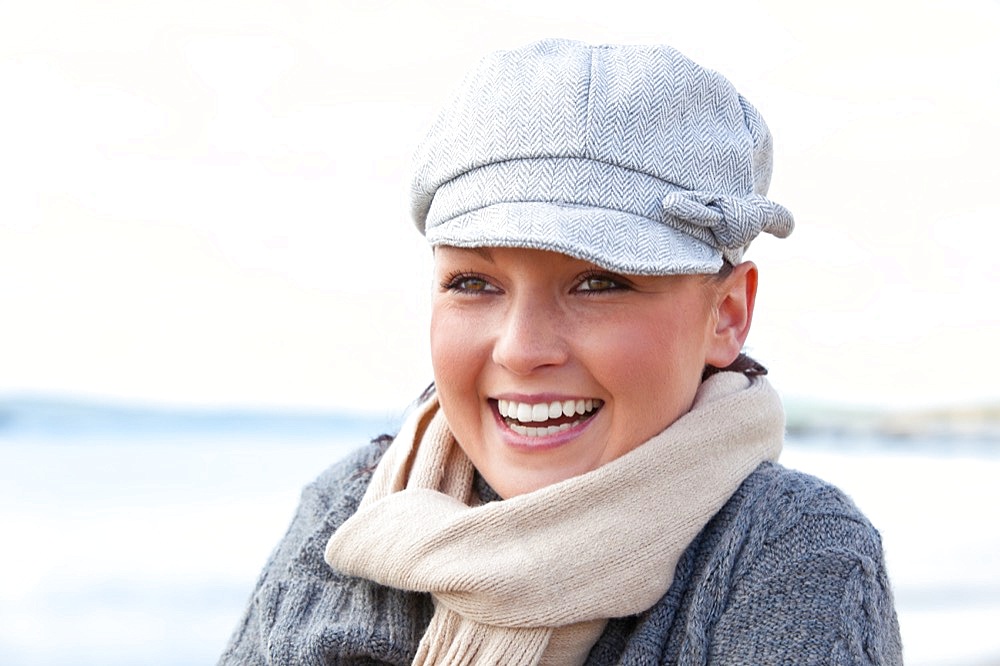 Pretty woman with scarf and hat standing on the beach