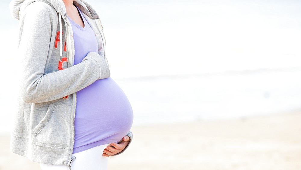 Pregnant young woman walking on the beach