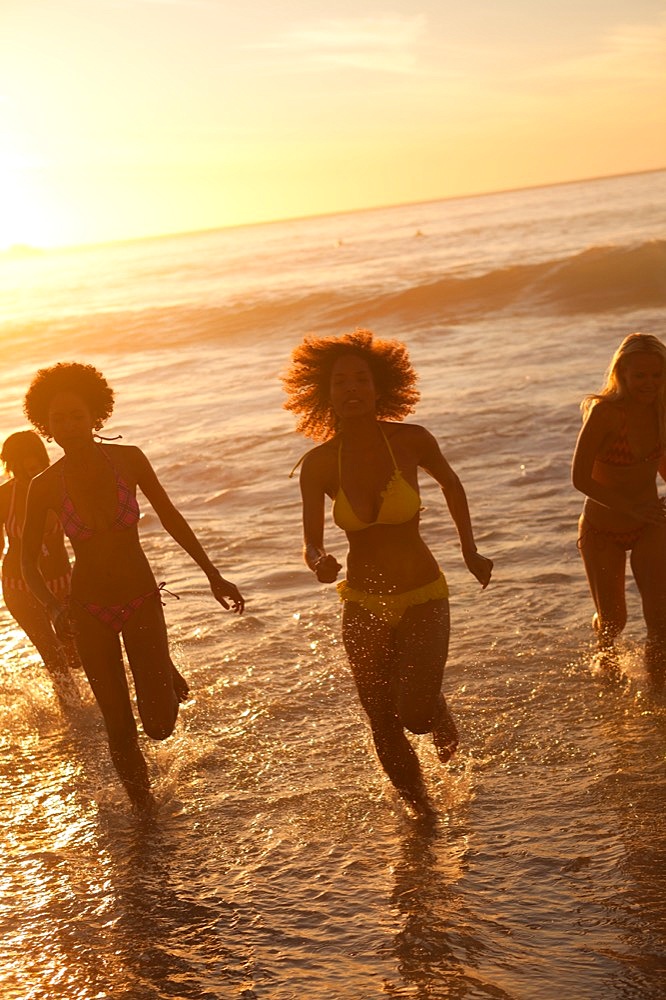 Four young women running in the water at sunset