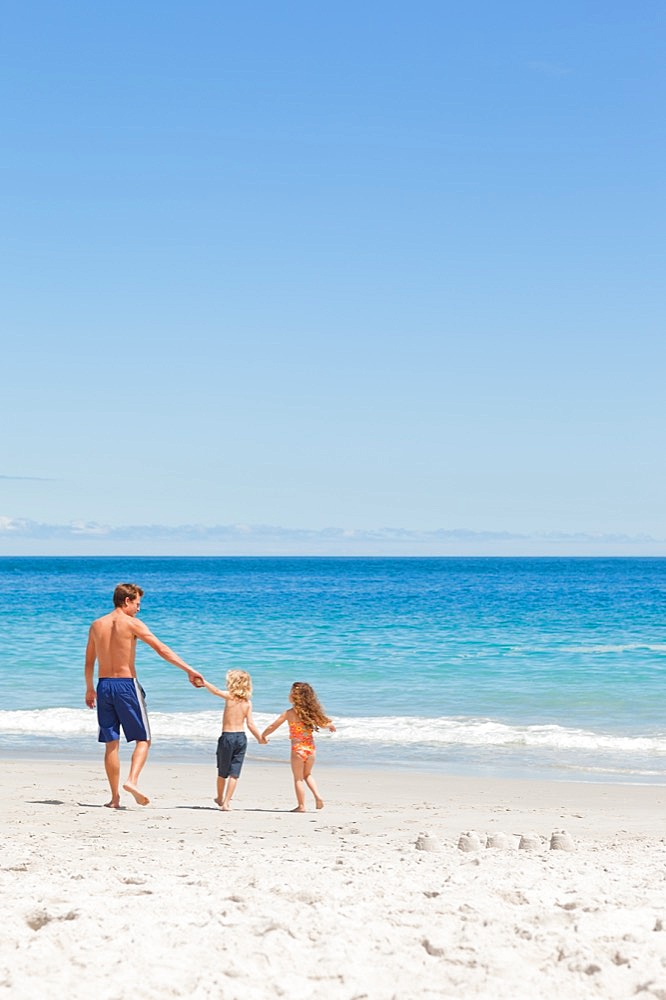 Young father walking with his children towards the sea