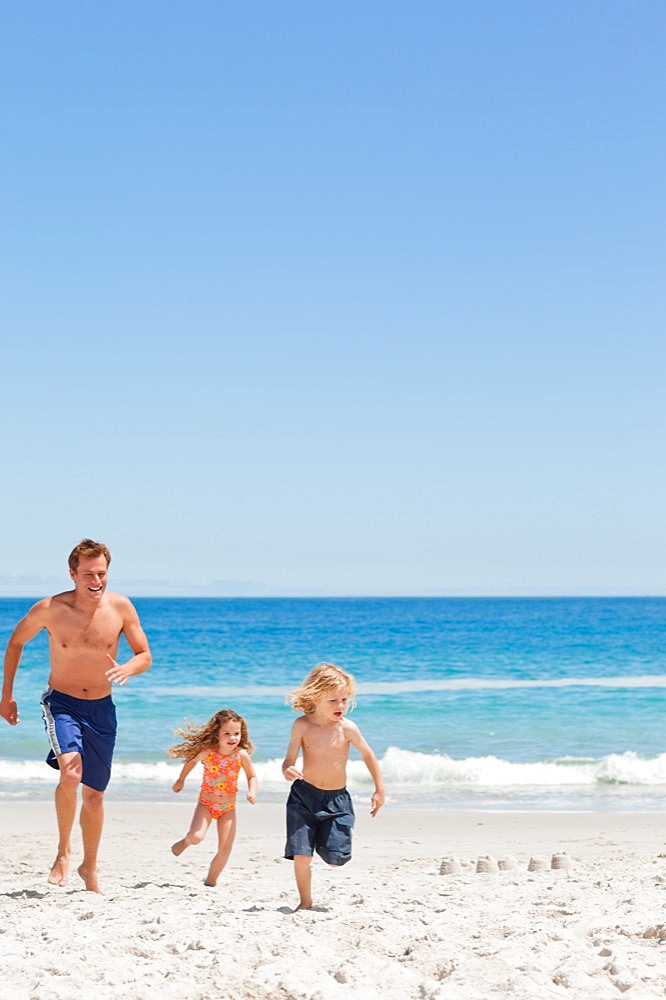 Young father running with his children on the beach
