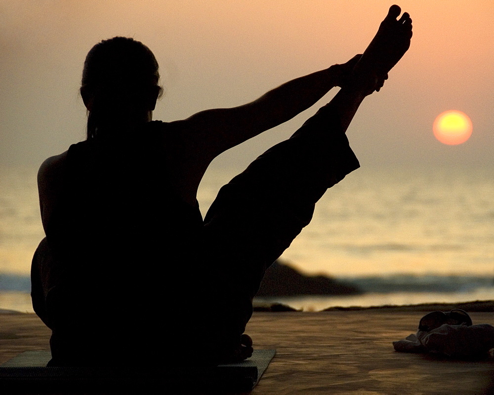 Young woman practicing Yoga at sunset on the beach, Goa, India