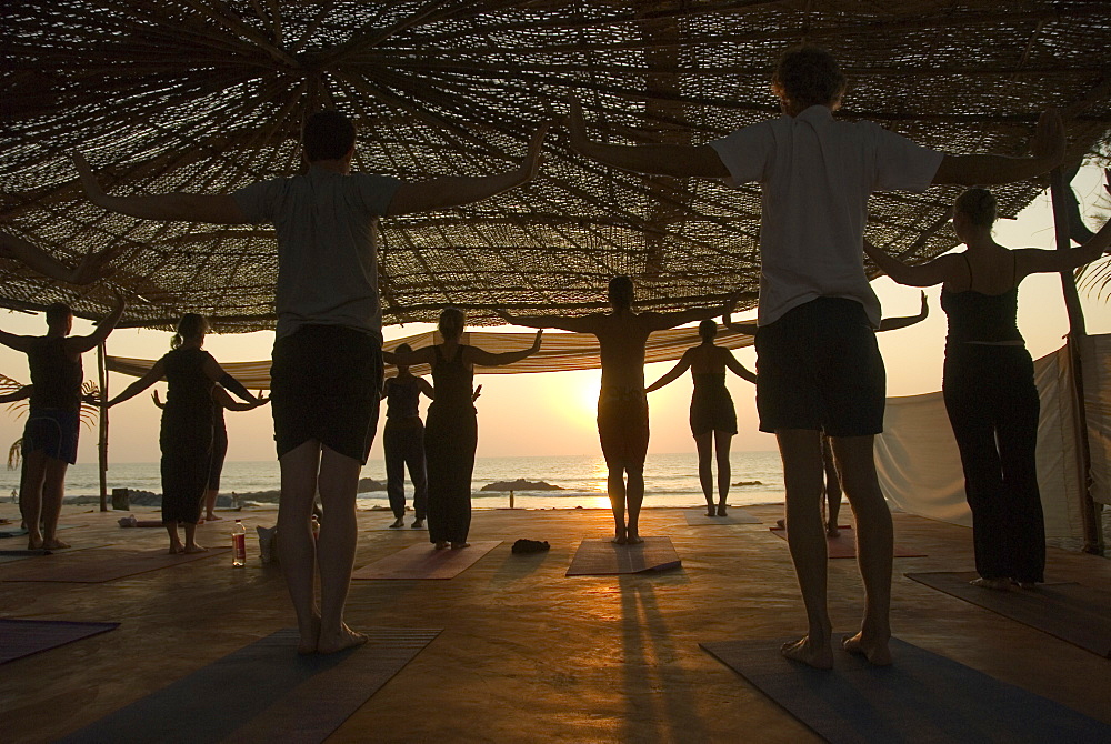 Group practicing Yoga at sunset on the beach, Goa, India