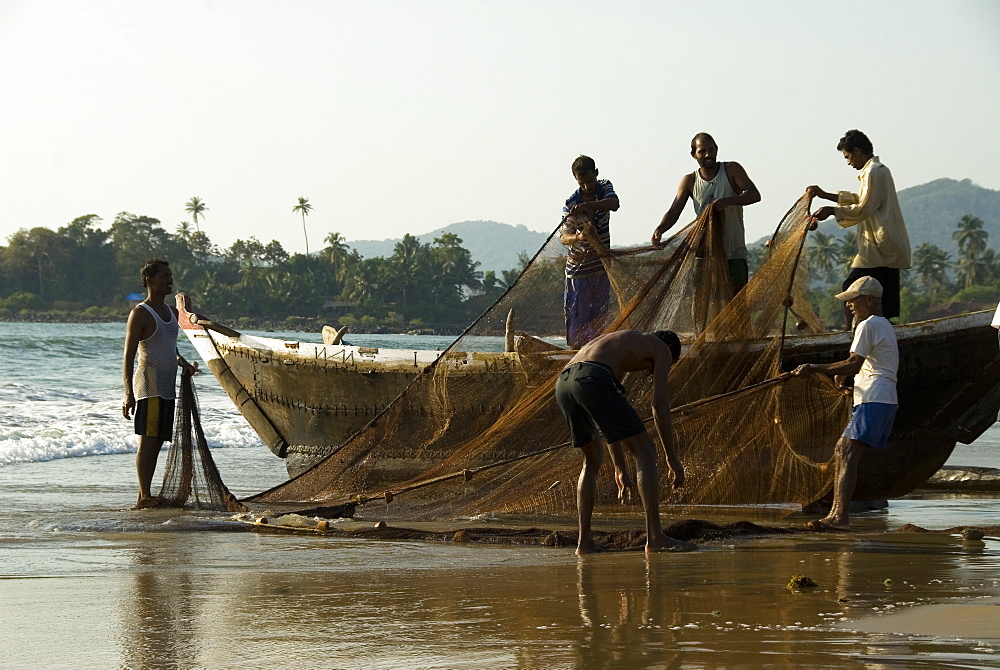 Fishermen untangling fishing nets on the beach after hauling in a catch, Goa, India