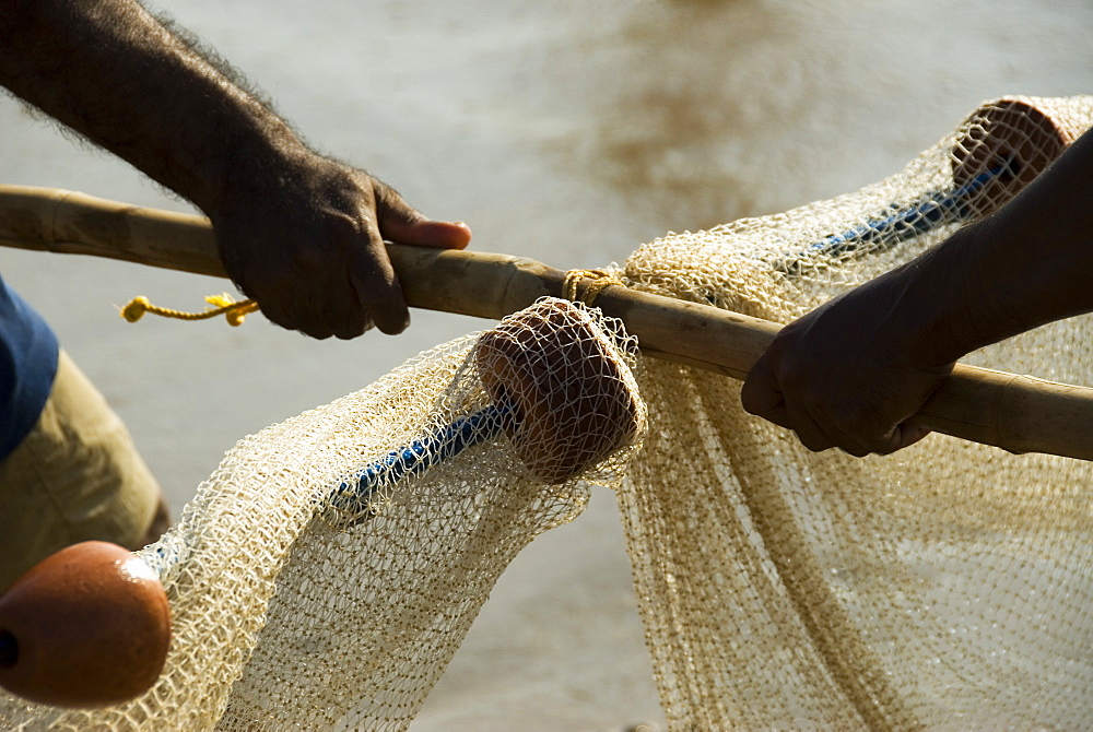 Close up of the hands of two men hauling in the fishing net from the beach, Goa, India