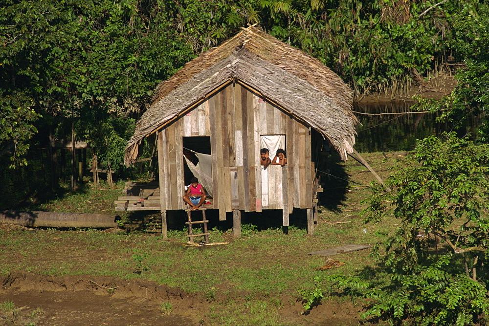 People waving from their thatched palm house on the waters edge, Caboclos, in the Breves Narrows in the Amazon area of Brazil, South America