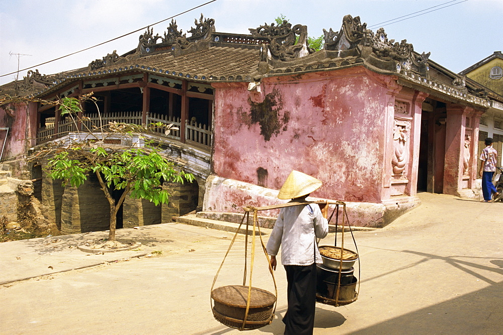 Woman carrying baskets on a pole by a covered bridge in Hoi An in Vietnam, Indochina, Southeast Asia, Asia