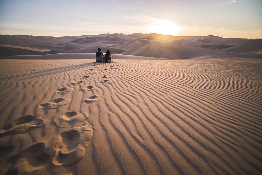 Couple watching the sunset over sand dunes in the desert at Huacachina, Ica Region, Peru, South America