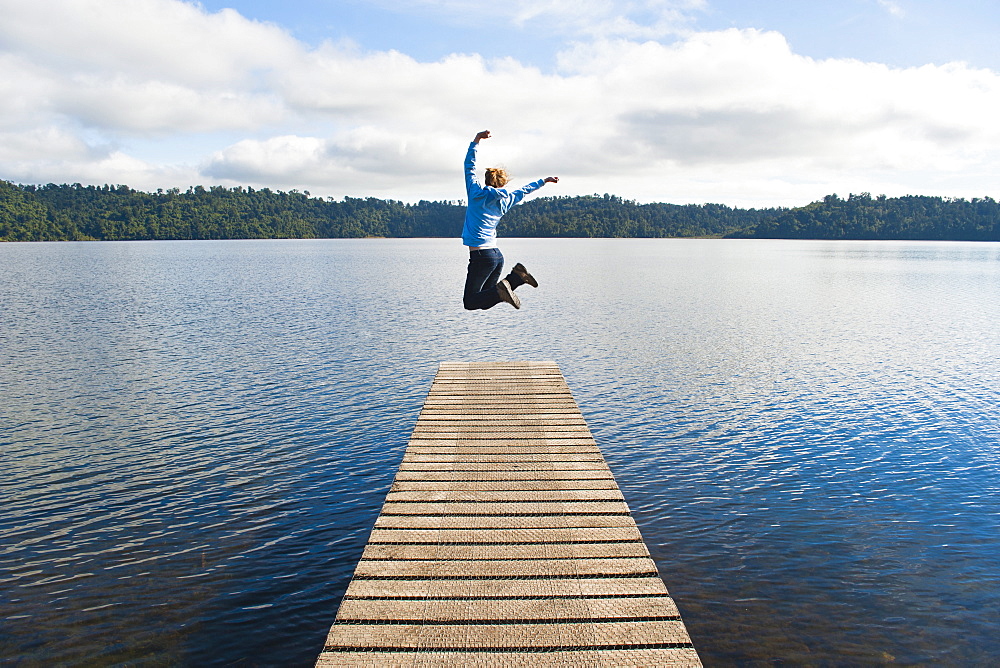 Woman jumping on a jetty at Lake Ianthe, West Coast, South Island, New Zealand, Pacific 