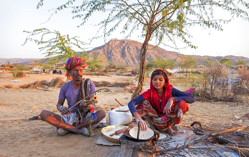 Hindu girl cooking while her father plays musical instrument in Pushkar, Rajasthan, India, Asia