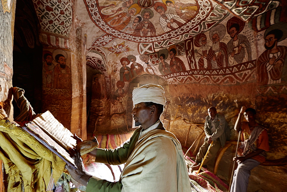 Priest reading in an old goatskin manuscript, Abuna Yemata Guh church with mural painting, Hawzien, Tigray Region, Ethiopia