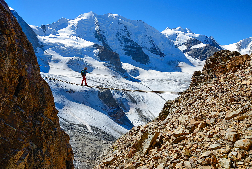 Woman on a suspension bridge climbing the via ferrata at Piz Trovat with view to Piz Palue (3905 m), Bellavista (3922 m) and Per