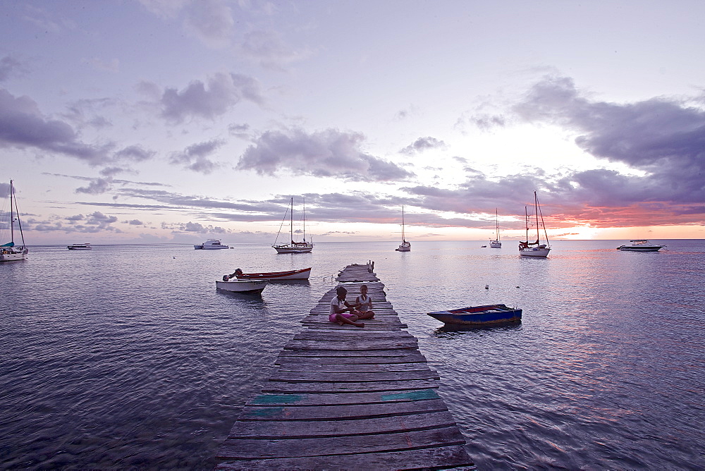 Children sitting on a wooden jetty at the sea in sunset, Dominica, Lesser Antilles, Caribbean