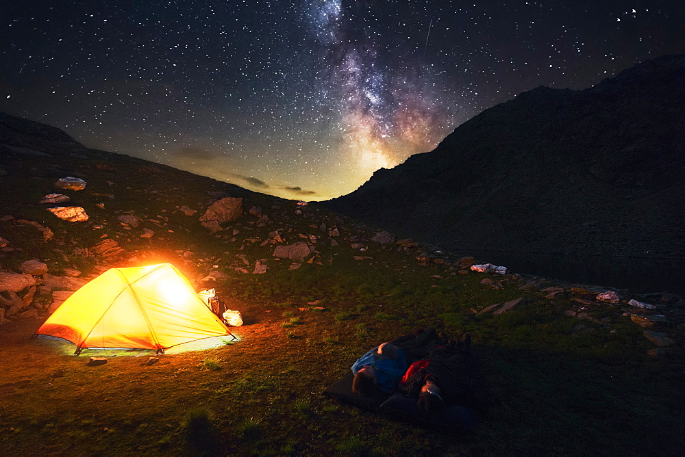 Two hikers watch the starry sky and milky way, camping spot in the Pfunderer Mountains, South Tyrol, Italy