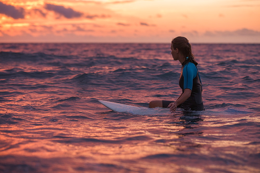 Young female surfer sitting on her surfboard in the water and waiting for a wave at sunset, Sao Tome, Sao Tome and Principe, Africa