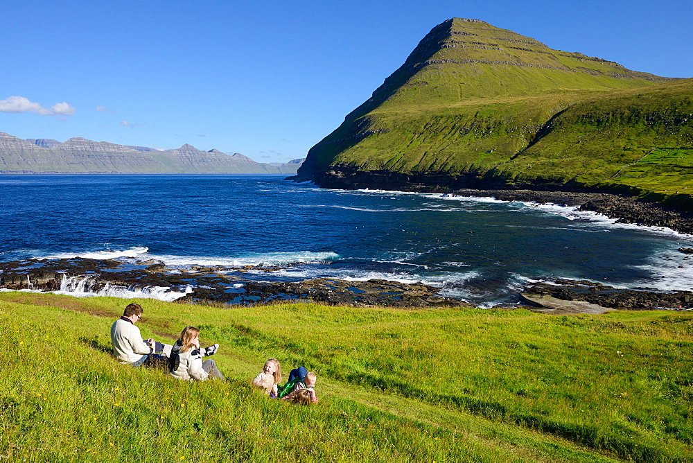 Family sitting on the grass overlooking the bay of Gjogv, Eysturoy Island, Faroe Islands