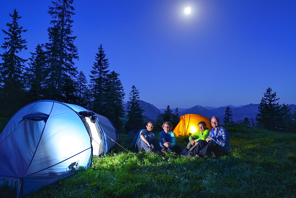 Four persons sitting in front of two illuminated tents, Blauberge, Bavarian Prealps, Upper Bavaria, Bavaria, Germany