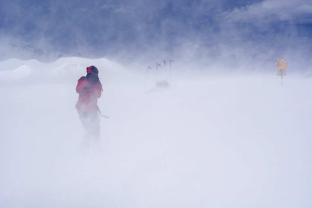 A backcountry skier with a DSLR camera taking a picture in a storm caused by Foehn winds, summit of the Mattjisch Horn, high valley called Fondei, Grison Alps, canton of Grison, Switzerland