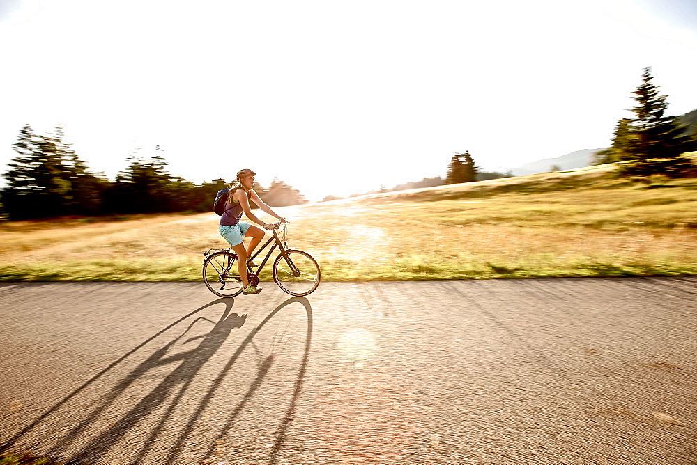 Young woman riding her bike near a meadow on a sunny day, Tannheimer Tal, Tyrol, Austria