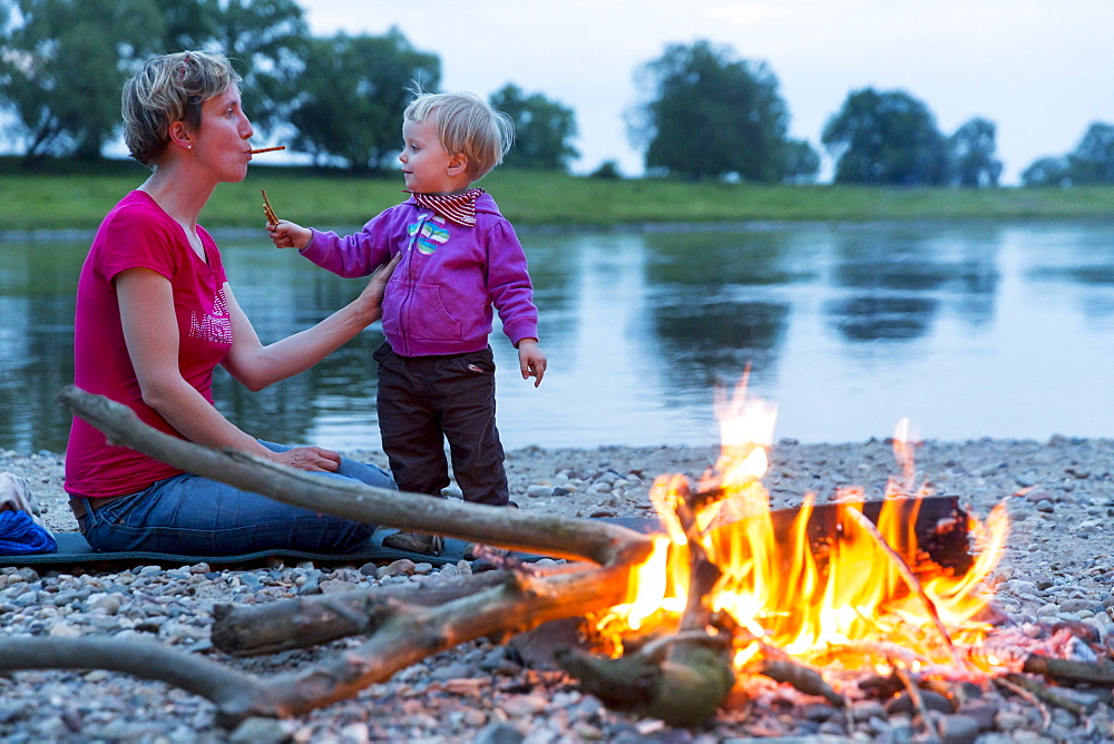 Mother and daughter making bread on a stick on the campfire, Camping along the river Elbe, Family bicycle tour along the river Elbe, adventure, from Torgau to Riesa, Saxony, Germany, Europe