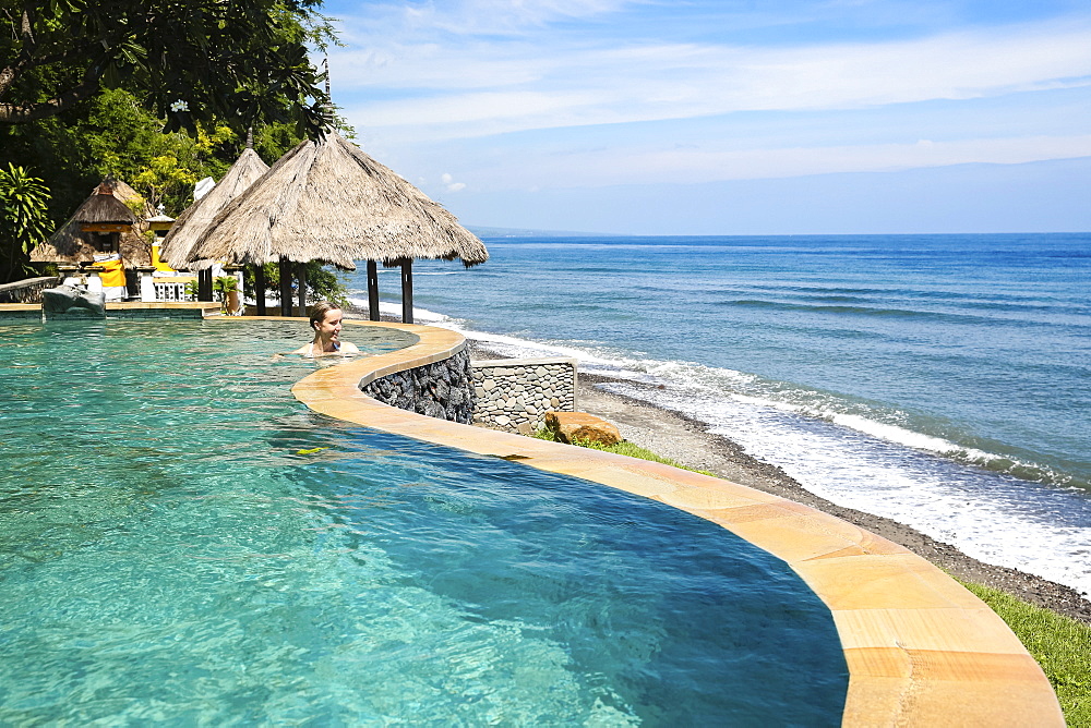 Woman in an infinity pool of a hotel with view to Indian Ocean, Amed, Bali, Indonesia