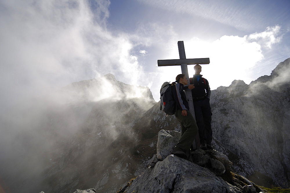 Hikers at a summit cross amidst some clouds, Wetterstein, Bavaria, Germany, Europe