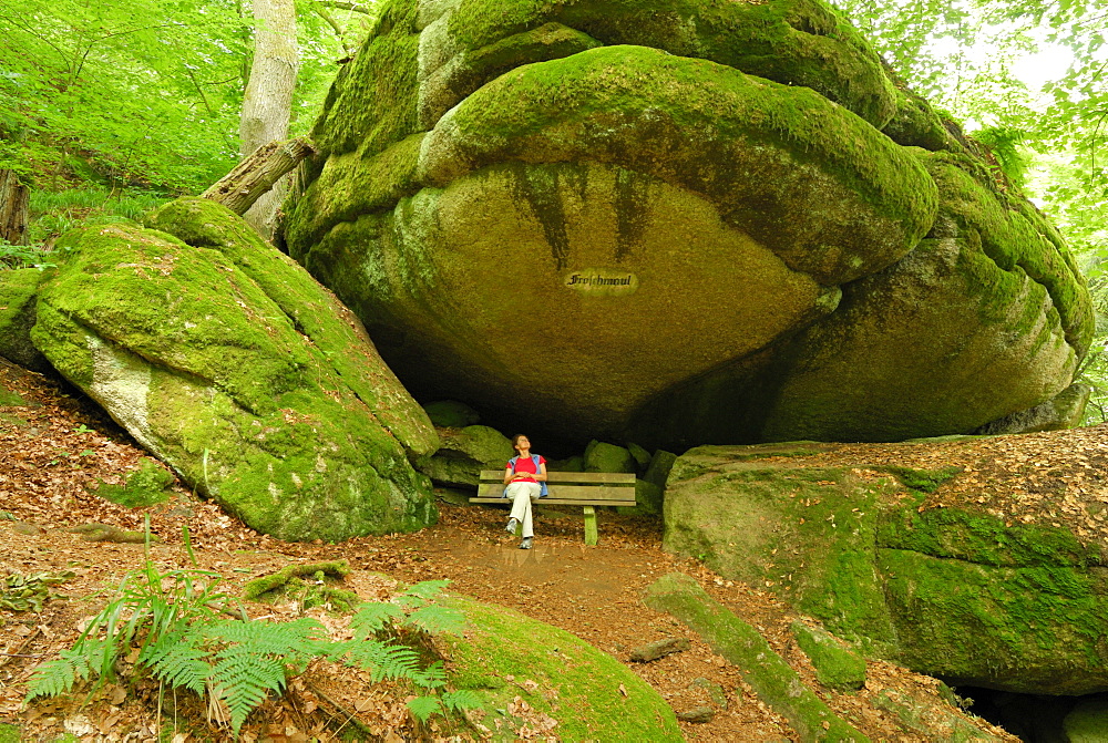 Woman sitting on a bench under a rock overhang, Felsenpark, castle Falkenstein, Bavarian Forest, Upper Palatinate, Bavaria, Germany