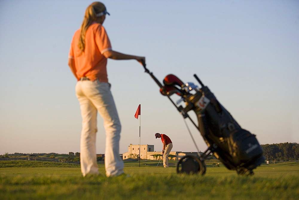 Male golfer preparing to hit ball, woman looking to him, Apulia, Italy