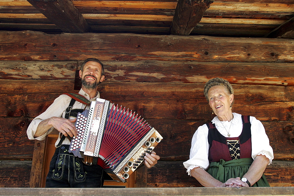 Mother and son sitting in front of log cabin, man playing Accordion, Salzburger Land, Austria