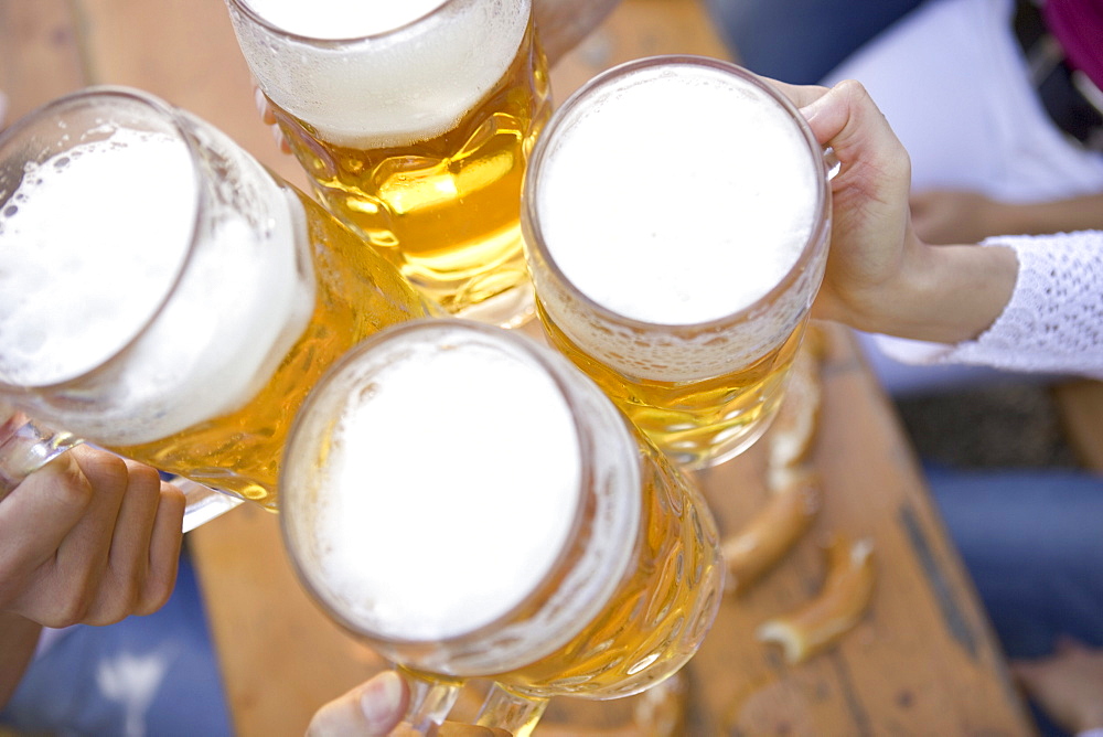 Four hands toasting with beer steins above table, Munich, Bavaria