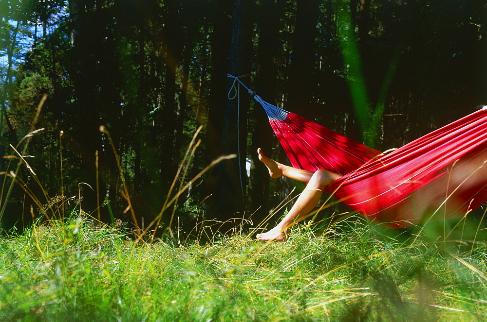 Young woman relaxing in hammock, legs hanging over side