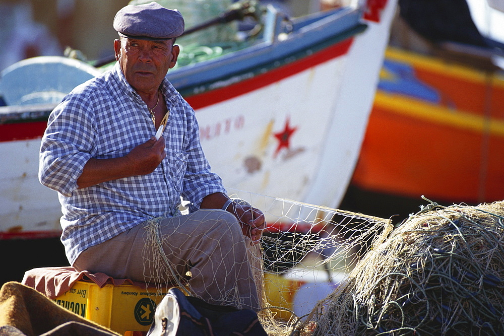 Fisherman repairing a fishing net at harbour, Algarve, Portugal, Europe