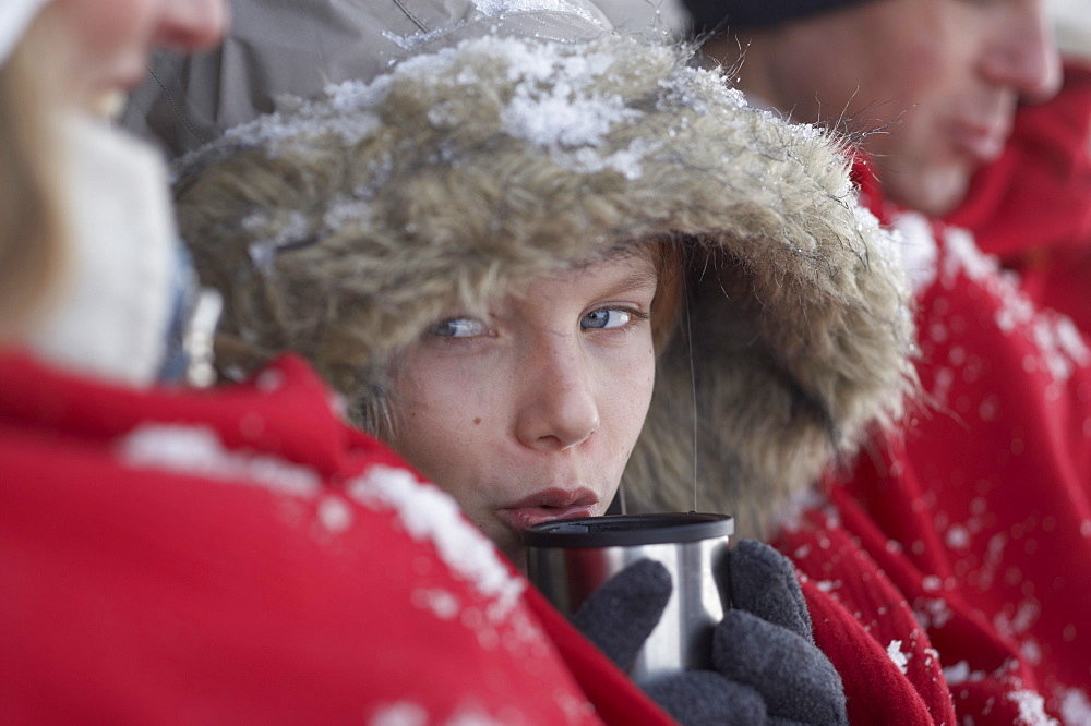 Parents and son leaning on wooden hut, warming with red blanket