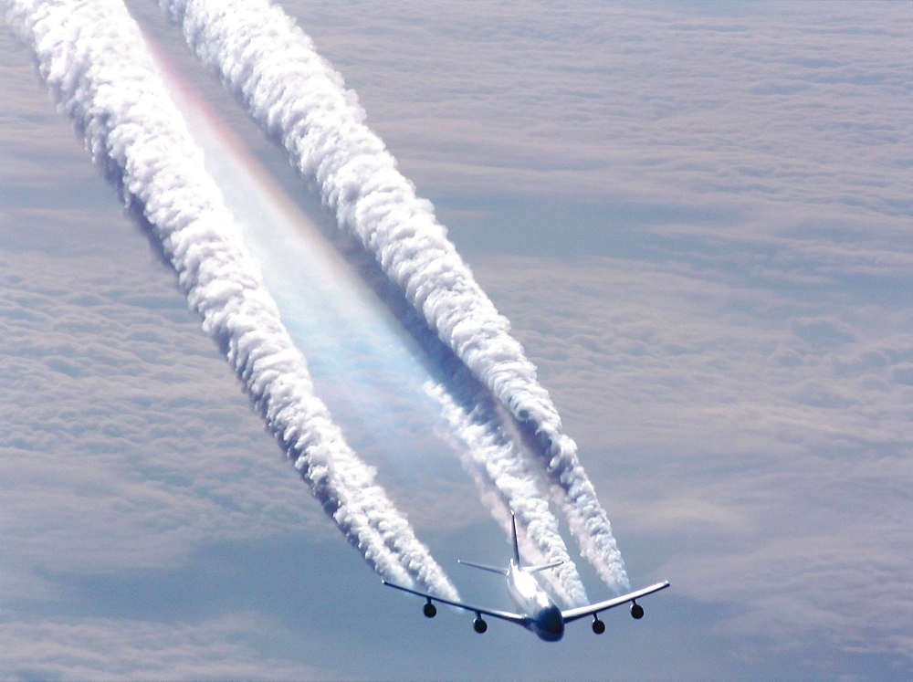 Plane flying over sea of clouds leaving huge condensation trails