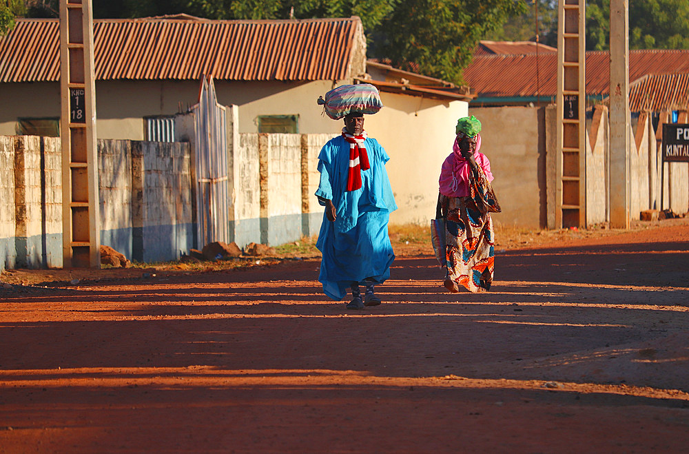 Gambia; Central River Region; Main street of Kuntaur; Married couple with luggage on their heads; Street scene in the morning sun;