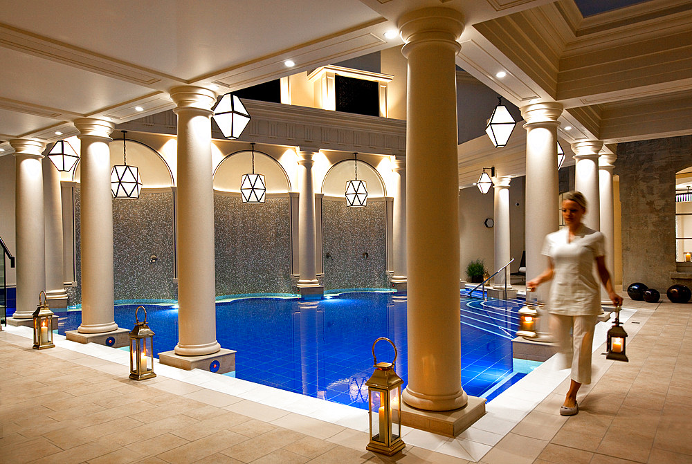 Evening shot of Spa therapist carrying lamps inside an intrioer pool room. Bath, United Kingdom