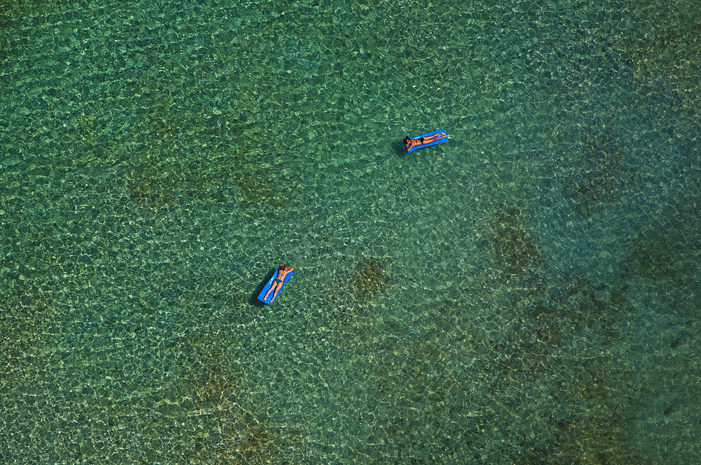 Two women floating on rubber floats in a clear blue ocean. Shot from the air. British Virgin Islands.