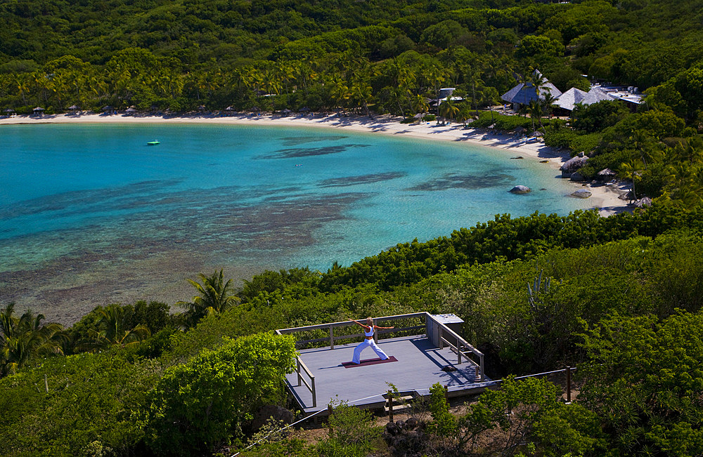 A woman performing exercises on a Yoga platform set up high over a bay with extended views of blue and green. British Virgin Islands.